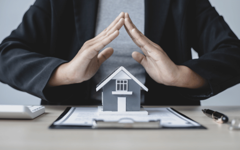 Mains qui forment un toit protecteur au-dessus d’une maison, symbolisant l'assurance emprunteur pour votre logement