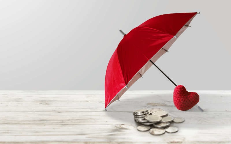 Parapluie rouge au-dessus de pièces de monnaie et d’une peluche en forme de cœur, symbolisant la couverture santé