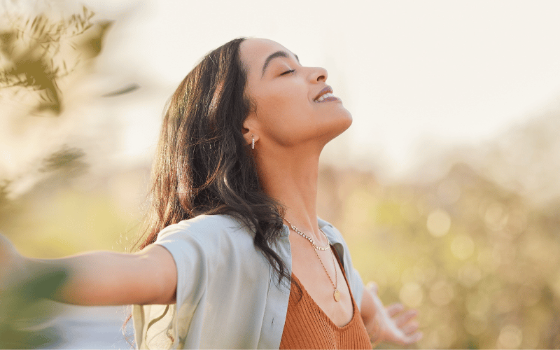 Jeune femme souriante, bras ouverts, respirant la liberté et la tranquillité grâce à une bonne mutuelle